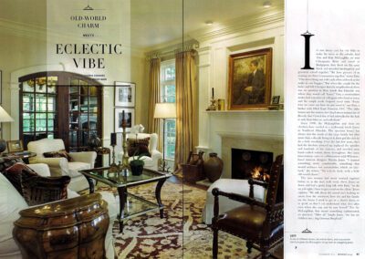 A magazine spread features a cozy, eclectic living room. The decor includes a mix of vintage and modern furniture, such as a plush white sofa, wooden chairs, a glass coffee table, and a patterned rug. There's a lit fireplace, artwork, and large windows with drapes.