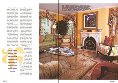 A magazine spread showcasing a living room designed with vibrant decor. The room features yellow walls, floral drapes, and a large ornate rug. It includes upholstered furniture with various patterns and colors, a fireplace with a decorative mantel, and large windows.