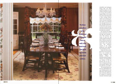 A formal dining room with a large wooden table surrounded by dark chairs. A chandelier hangs above the table, which is set with flowers and candles. Floral curtains frame the windows, and the room features patterned wallpaper and a coordinating rug.