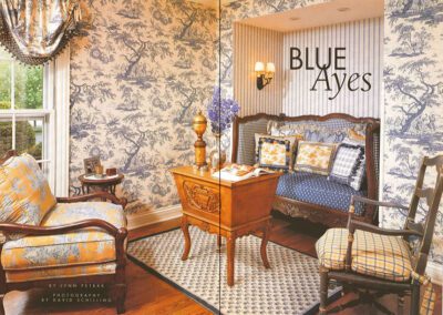 A room with blue and white toile wallpaper, wooden furniture, and a small bed with blue and yellow bedding. There's a wooden desk with decorative items and a vase with flowers. The window has draped curtains, and the text "BLUE Ayres" is displayed on the wall.